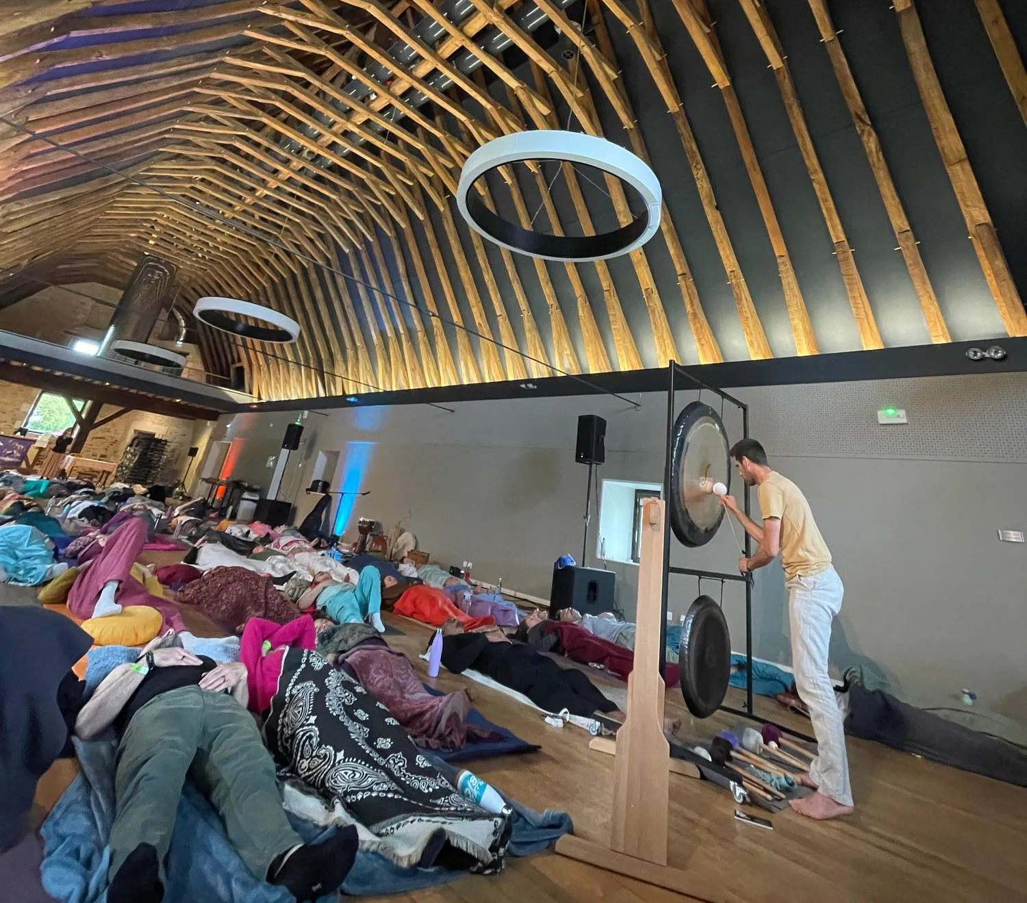 Public allongé dans une grange sous une charpente de bois clair pendant un concert respiratoire