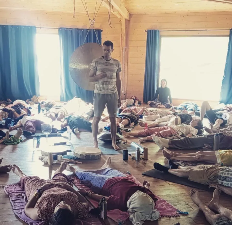 Groupe allongé dans une salle en bois clair, un gong suspendu au premier plan